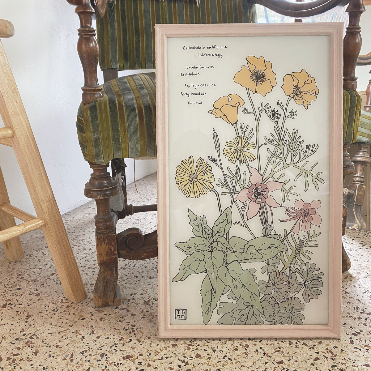 Framed painting of desert plants propped against antique chair